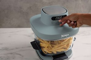 Ninja amplia il suo sistema di friggitrici ad aria in vetro con la nuova Ninja CRISPI PRO 6 JPG R AS101UKGY InUse Kitchen Counter UI Closeup Hand